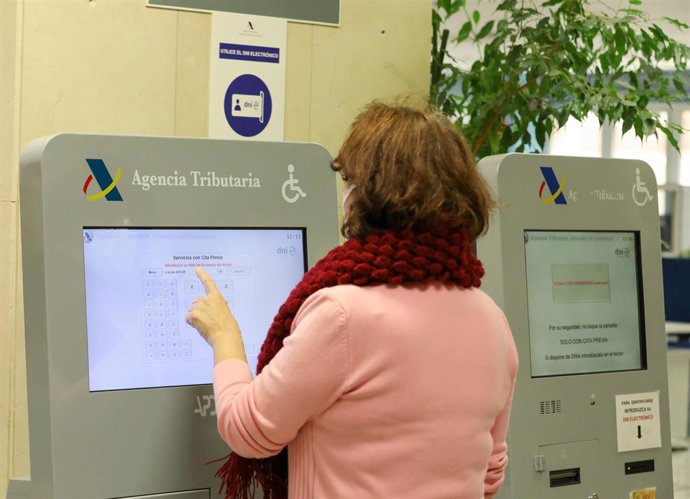 Archivo - Una mujer recoge su turno en una oficina de la Agencia Tributaria. Archivo.