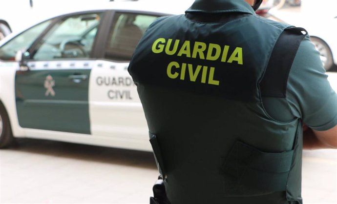 Archivo - Un agente de la Guardia Civil, de espaldas, junto a un vehículo oficial.