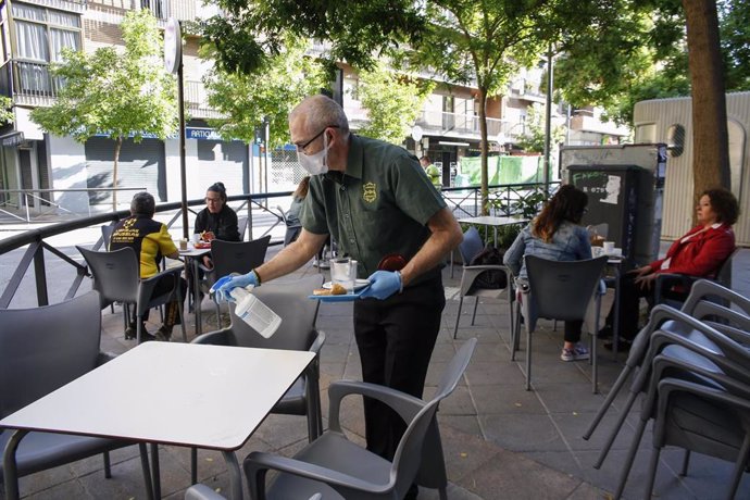 Archivo - Un camarero limpiando una mesa del bar, en una foto de archivo.