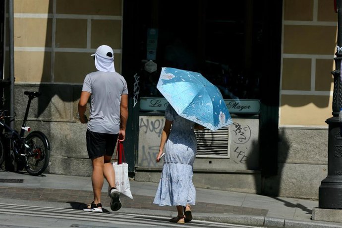 Una pareja camina con una gorra y un paraguas el día en que España ha comenzado a sufrir un "importante" episodio cálido con temperaturas de pleno verano, a 17 de mayo de 2022, en Madrid (España). Algunas zonas de la península rozarán los 40 grados cent