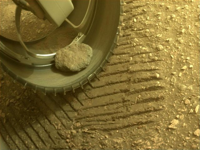 La roca capturada en febrero todavía en la rueda delantera izquierda del rover en sol 449, imagen adquirida el 26 de mayo de 2022 (Sol 449).