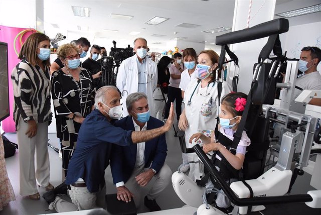 El piloto Carlos Sainz y el presidente de Fundación Aladina, Paco Arango, junto a Valeria, una niña usuaria del sistema 'Lokomat infantil' en el Hospital Nacional de Parapléjicos