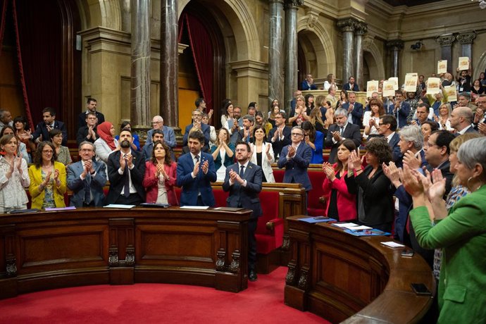 Els diputats del PSC, ERC, Junts i els comuns aplaudeixen al Parlament i la CUP ensenya cartells en defensa de la llengua després de l'aprovació de la llei del catal a l'escola.