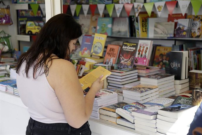 Archivo - Una mujer ojea un ejemplar en una feria del libro.