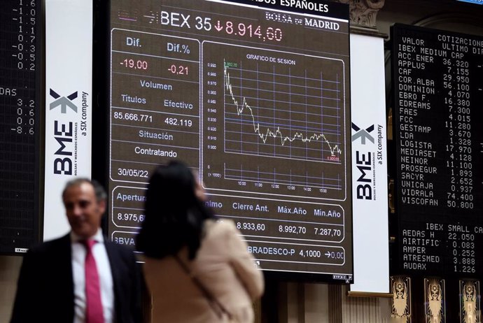 Dos personas frente a un panel de valores del Ibex 25 en el Palacio de la Bolsa, a 30 de mayo de 2022, en Madrid (España). El Ibex 35 ha retrocedido un 0,14 % en la media sesión de este lunes, hasta situarse en los 8.920, 9 puntos en una jornada marcada