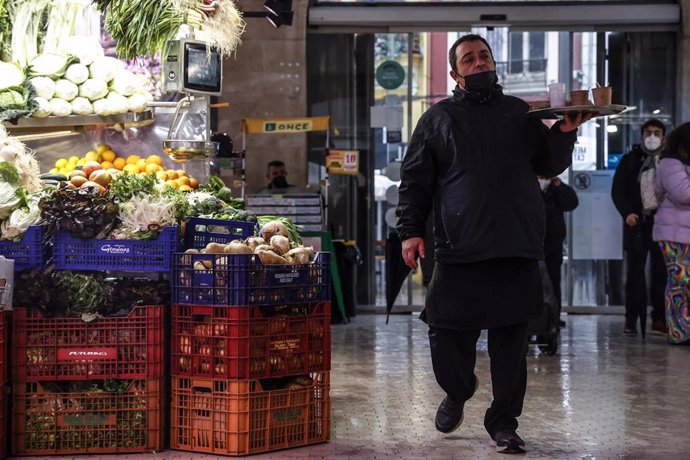 Archivo - Un camarero pasa por un puesto de fruta y verdura en un mercado  