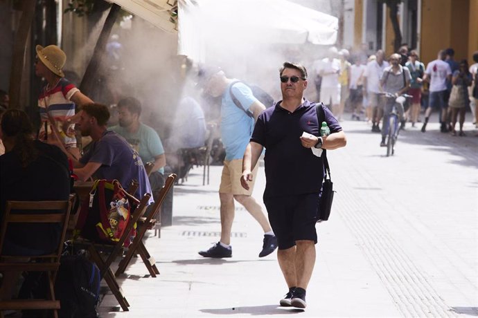 Un señor pasa por debajo de unos aspersores instalados en un bar por las altas temperaturas en Sevilla