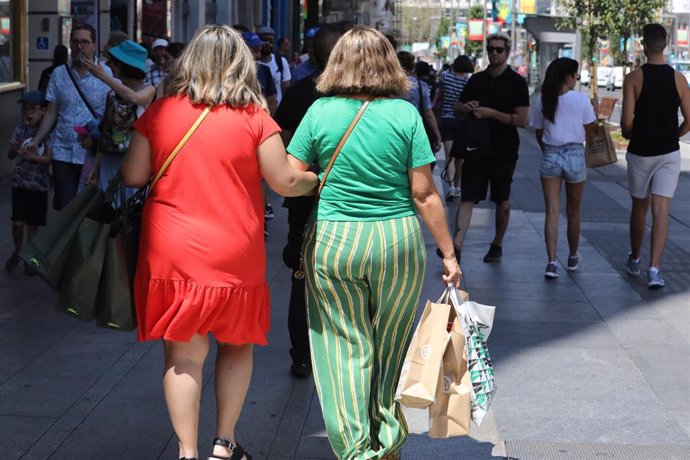 Archivo - Dos mujeres pasean cogidas del brazo, con bolsas en la mano, en una calle