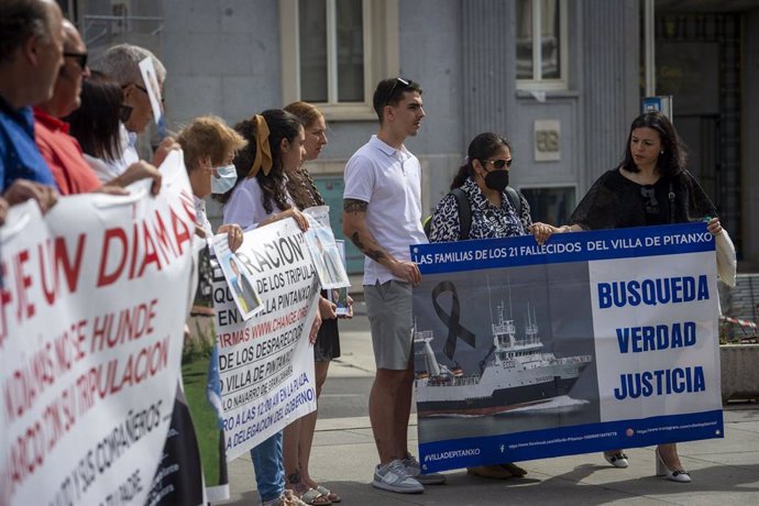Familiares de marineros fallecidos sostienen pancartas y fotografías en una concentración, a las puertas del Congreso de los Diputados.