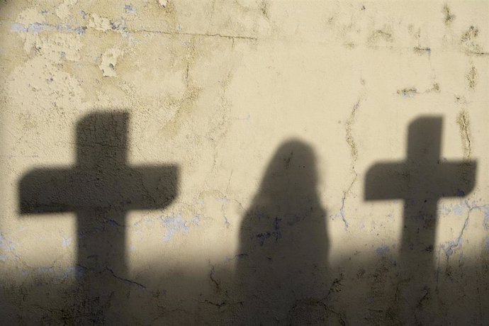 Archivo - Sombra de una mujer y dos cruces en un cementerio.