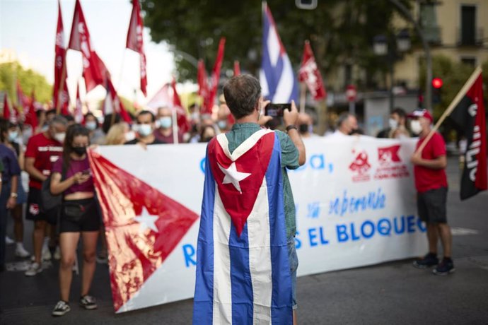 Archivo - Una persona con la bandera de Cuba en la espalda saca una fotografía a una gran pancarta en una manifestación contra el embargo económico de Estados Unidos sobre Cuba, a 24 de julio de 2021, en Madrid (España). 
