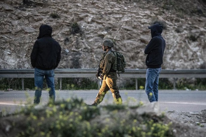 Archivo - 03 April 2022, Palestinian Territories, Hebron: An armed Israeli soldier (C) walks past two Palestinians after Israeli soldiers were deployed to prevent Palestinian workers from crossing illegally into Israel through an opening in the separati