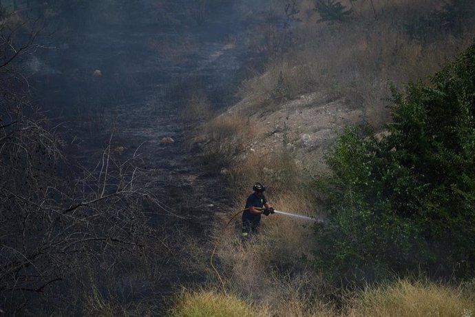 Un bombero sofoca el fuego con una manguera tras el incendio de pastos ocasionado en el Espacio Ibercaja del barrio de Delicias.