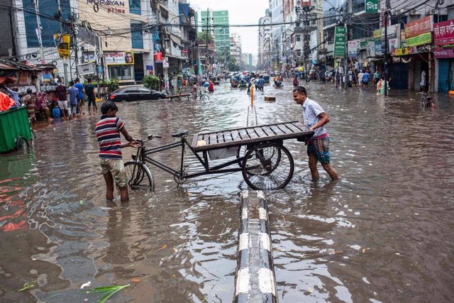 Archivo - Dos hombres intentan mover su bicicleta de tres ruedas a través de la inundada Green Road en Dhaka tras las fuertes lluvias. (ARCHIVO)