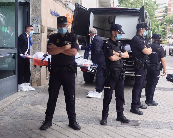 Un operario transporta el cuerpo de una de las tres personas muertas a balazos, junto a varios agentes de la Policía Nacional que custodian el portal donde han sucedido los hechos, en el número 205 de la calle Serrano, a 20 de junio de 2022, en Madrid (