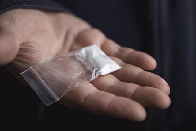 Archivo - Mano de hombre sosteniendo un paquete de plástico on polvo de cocaína u otras drogas.