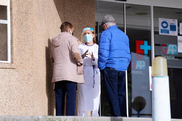 Archivo - Una sanitaria atiende a dos personas a la entrada del Centro de Salud de Cazoña. Archivo