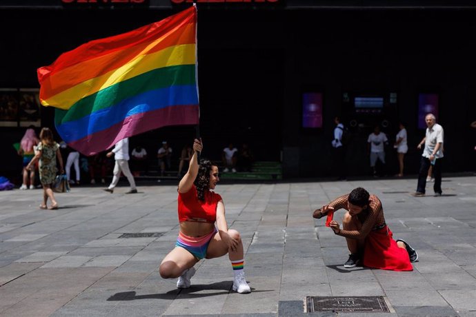 Un hombre toma una fotografía a una mujer que posa con una bandera LGBT, en la plaza de Callao.