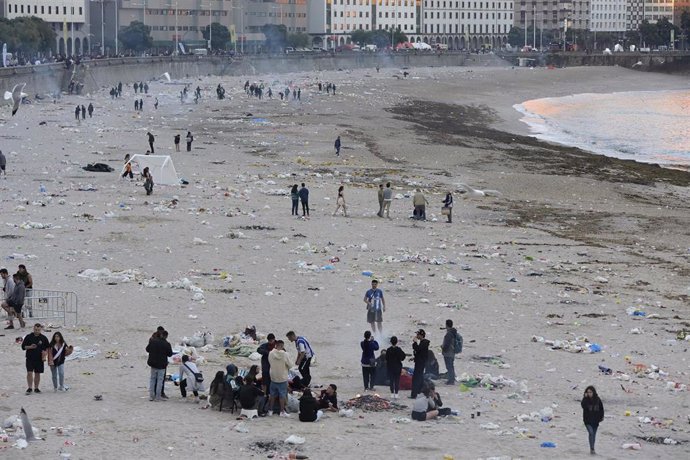 Vista general de la playa de Orzán con grupos de personas y restos de basura después de la celebración de las hogueras de la noche de San Juan.