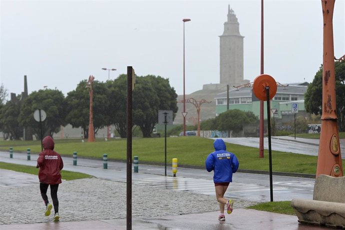 Dos personas corren con chubasqueros cerca de la torre de Hércules, a 19 de junio de 2022, en A Coruña, Galicia, (España). 