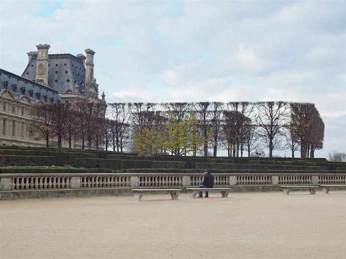 Archivo - Una persona sentada en un banco frente al Museo del Louvre de París