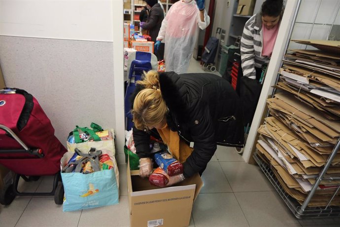 Archivo - Una mujer coloca en una caja los productos que va a adquirir en el economato solidario de Cáritas de Madrid.