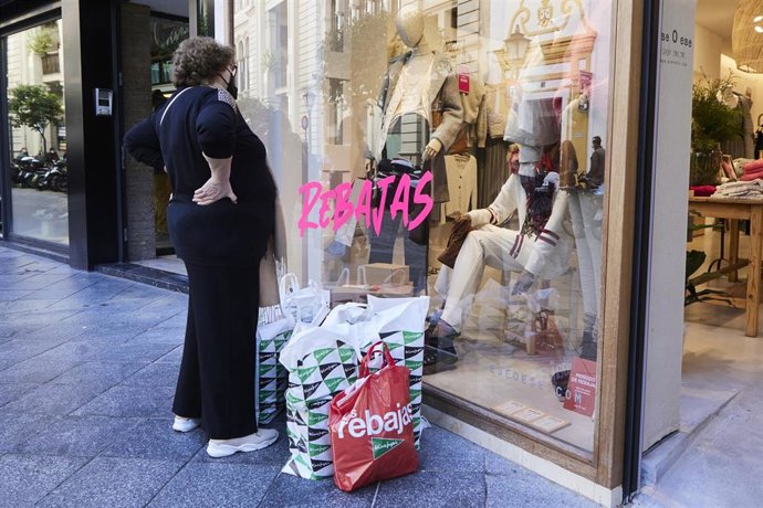 Archivo - Una mujer observa un escaparate con muchas bolsas de compras en el suelo durante un día de rebajas, en foto de archivo.