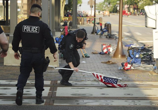 05 July 2022, US, Chicago: A police officer picks up a national flag left behind at the scene where an unknown perpetrator fired shots during a Fourth of July parade in Highland Park, killing at least six people and injuring 24. Photo: Stacey Wescott/Chic