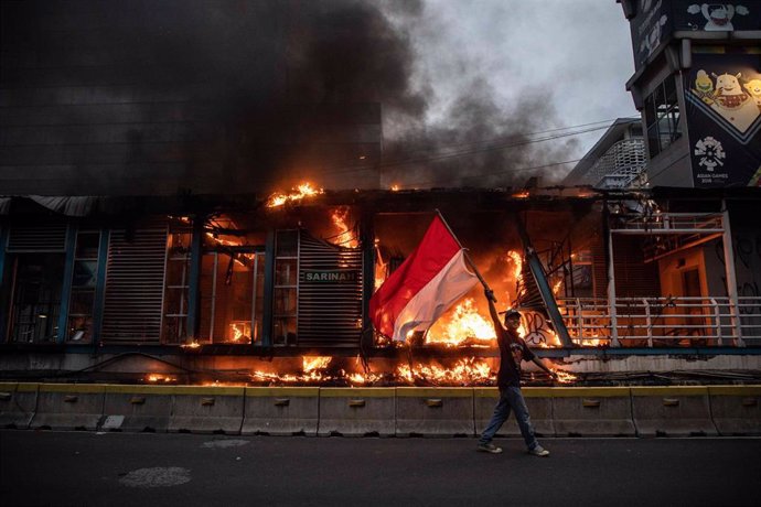 Archivo - Un manifestante agita la bandera indonesia mientras pasa por delante de un inmueble en llamas durante una manifestación contra un proyecto de ley ómnibus del gobierno sobre la creación de empleo que, según ellos, privará a los trabajadores de 