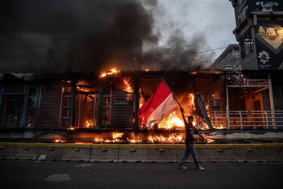 Archivo - Un manifestante agita la bandera indonesia mientras pasa por delante de un inmueble en llamas durante una manifestación contra un proyecto de ley ómnibus del gobierno sobre la creación de empleo que, según ellos, privará a los trabajadores de