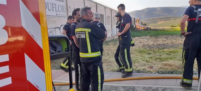 Bomberos con el incendio de la nave al fondo