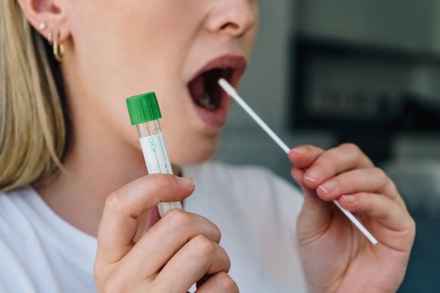 Archivo - Mujer joven sostiene un hisopo en la boca y sostiene un tubo médico para la prueba de coronavirus