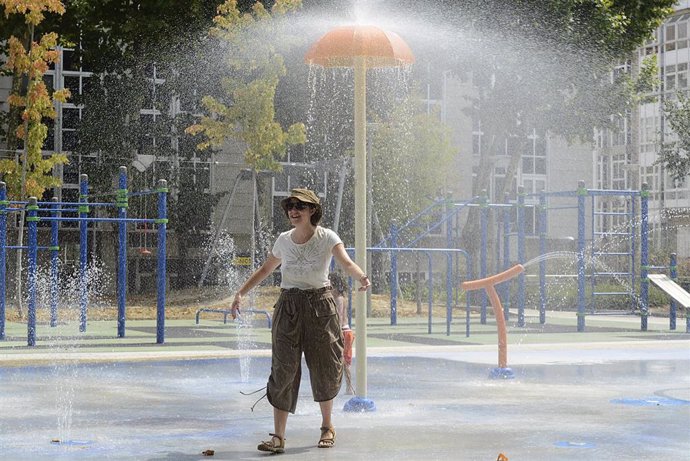 Una mujer se refresca en unos chorros de un parque.
