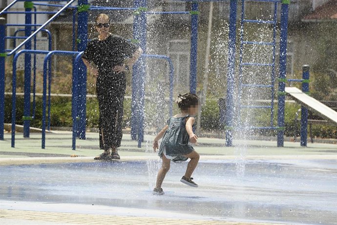 Dos personas se refrescan en unos chorros durante un día de la ola de calor. 