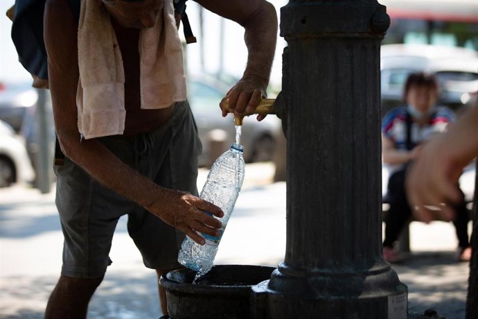Un hombre rellena una botella de agua en una fuente en el parque de la Barceloneta