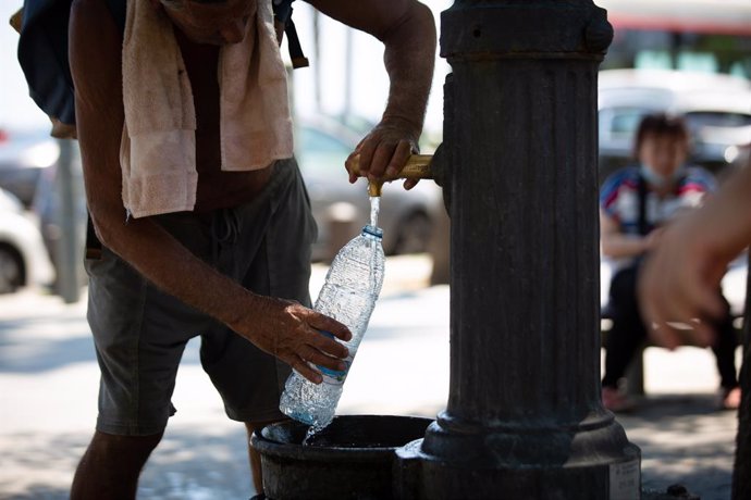 Un home emplena una ampolla d'aigua en una font al parc de la Barceloneta (Barcelona)