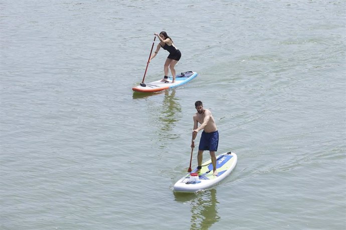 Archivo - Dos personas practican padel surf por el río Guadalquivir 