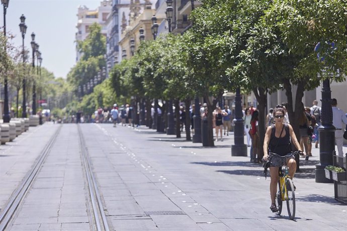 Una ciclista circula por la avenida de la Constitución desierta de peatones en el primer día de la segunda ola de calor, a 7 de julio de 2022 en Sevilla (Andalucía, España)