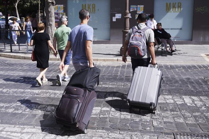 Dos turistas, con maletas, cruzan un paso de peatones.