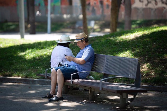 Un hombre mira su teléfono móvil en un banco bajo la sombra 