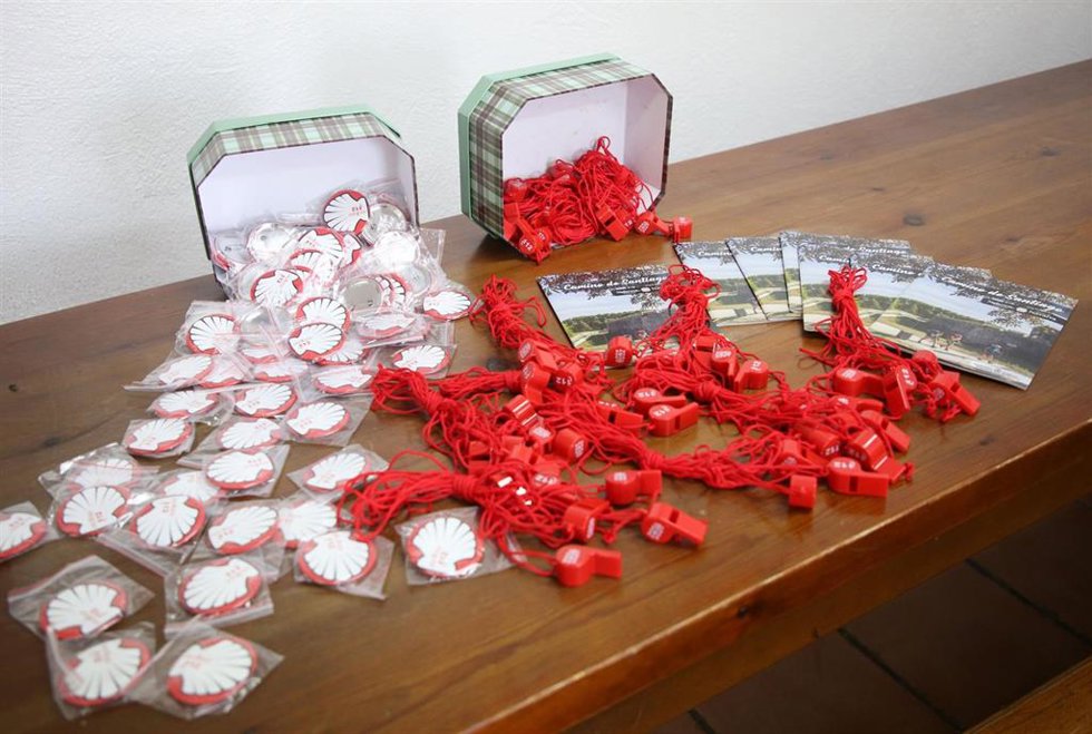 Silbatos y chapas que serán repartidos en albergues y oficinas de turismo.