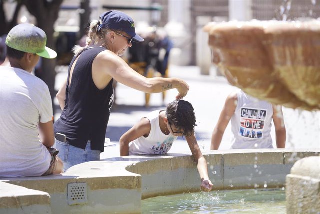 Una madre le echa agua a su hijo, por la cabeza, en la fuente de la plaza Virgen de los Reyes en el primer día de la segunda ola de calor, a 7 de julio de 2022 en Sevilla (Andalucía, España)