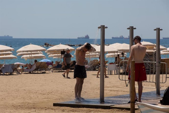 Varias personas se mojan en las duchas de la playa de la Barceloneta, a 13 de julio de 2022, en Barcelona, Catalunya (España). 