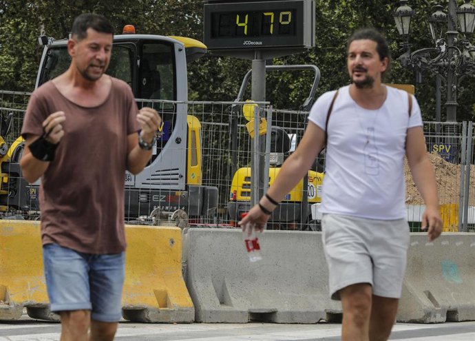 Archivo - Dos hombres pasan junto a un termómetro que marca 47 durante un día de alerta roja por altas temperaturas