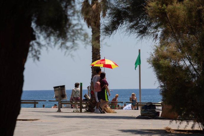 Dos personas se protegen del sol con una sombrilla en la playa de la Barceloneta, a 13 de julio de 2022, en Barcelona, Catalunya (España). 