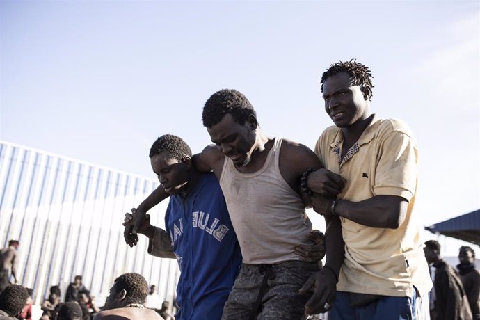 Archivo - Un migrante es ayudado por sus compañeros, tras conseguir saltar la valla de Melilla, en una foto de archivo.