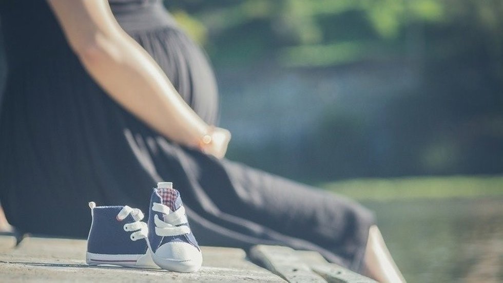 Una mujer embarazada junto a unas zapatillas de bebé.