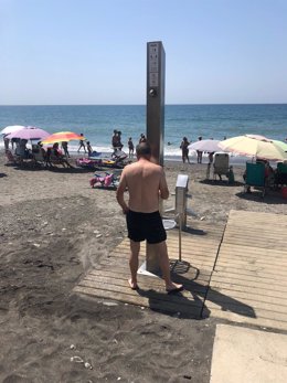 Un usuario de la playa de Algarrobo (Málaga) junto a una de las duchas de la playa. A 31 de julio de 2022.