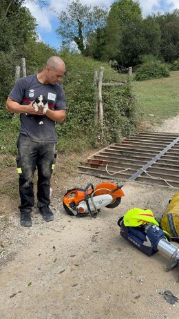 Un bombero del 112 con el cachorro rescatado en sus manos y junto al paso canadiense en que cayó el animal