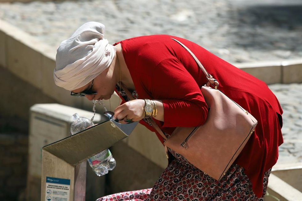 Una mujer bebe agua de una fuente para combatir el calor.